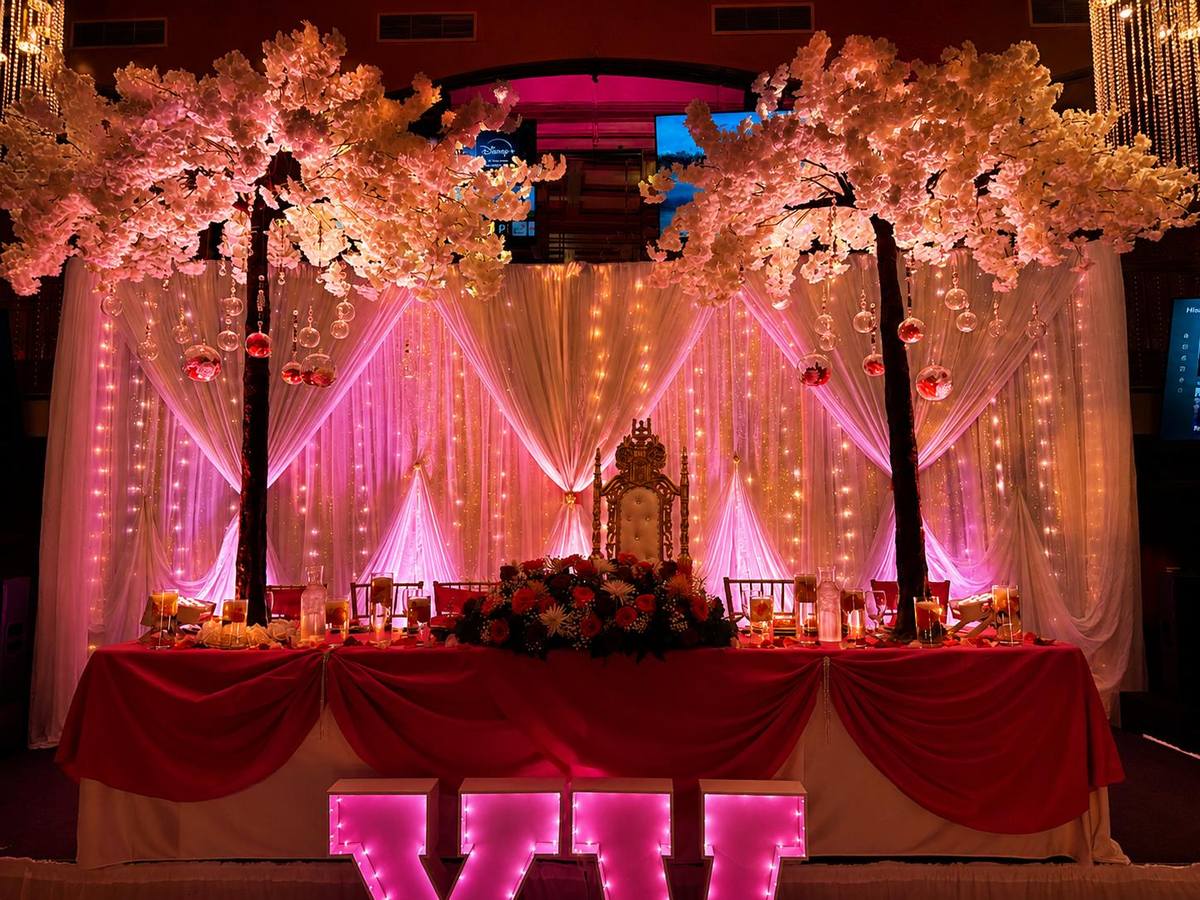 Mesa principal de quinceañera montada por D'Angelli: trono dorado, cortinas de luces y árboles de flores