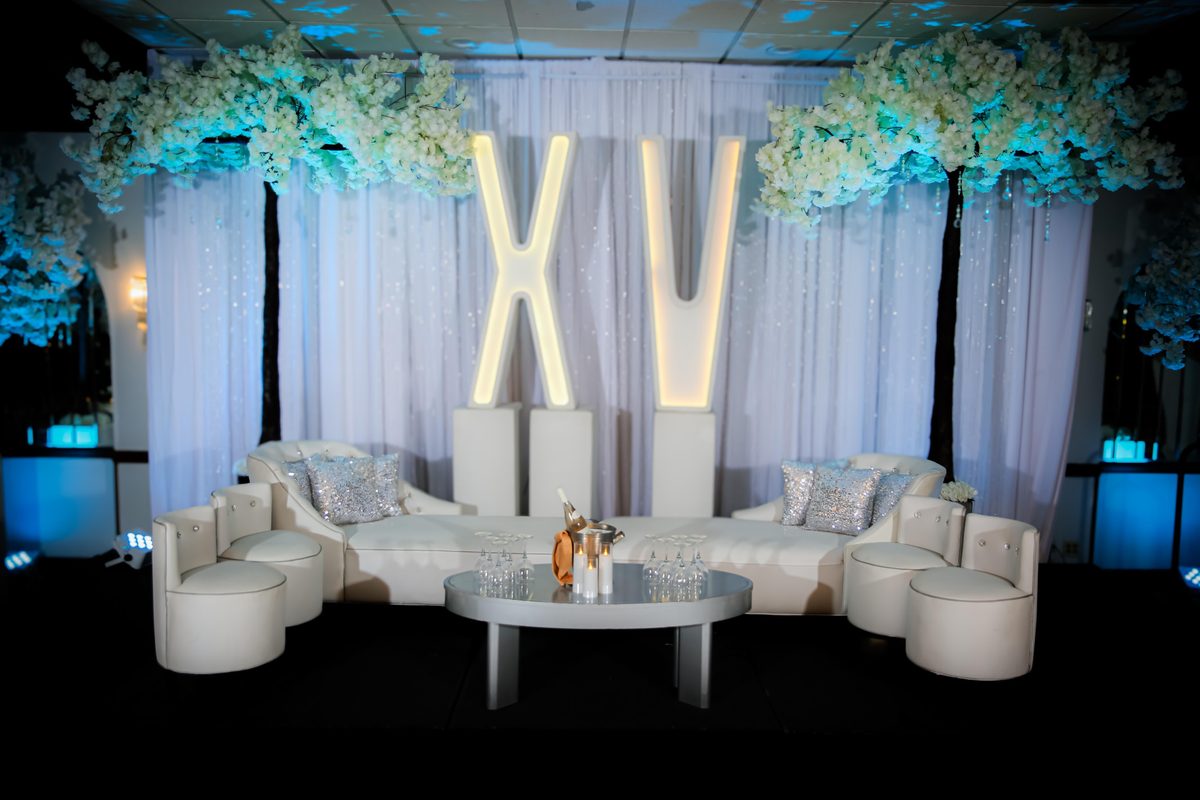 Letras XV iluminadas, lounge blanco y árboles de flores